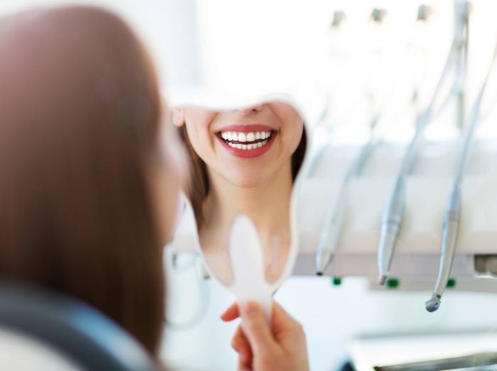Woman looking at smile in mirror after cosmetic dentistry