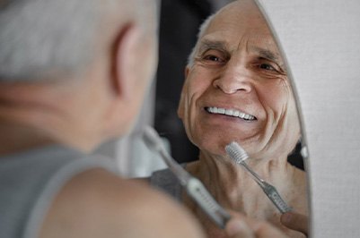 Man looking in mirror as he brushes his dental implants