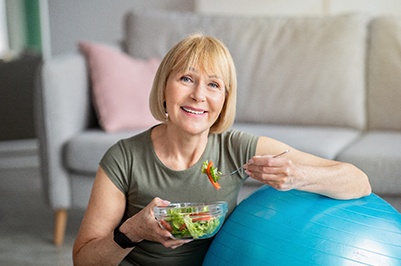 Woman in a green t-shirt sitting against an exercise ball eating a salad