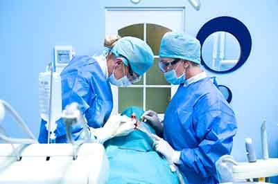 Patient undergoing procedure performed by two dentists in blue scrubs