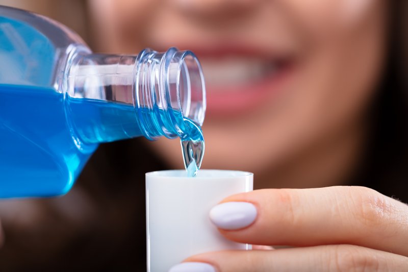 A woman pouring fluoridated mouthwash into a large cap