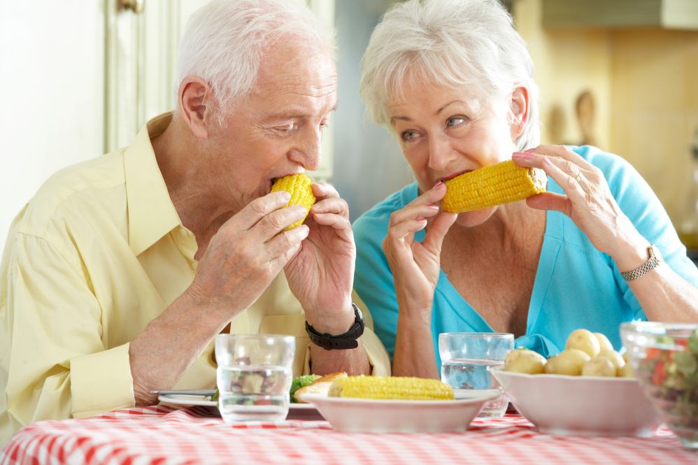 An older couple eating corn on the cob.